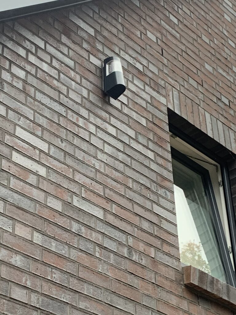 Backsteinfassade mit einem modernen Außenlicht und einem teilweise geöffneten Fenster.